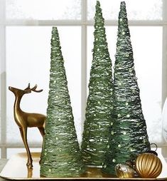 there are three small trees on the tray next to a deer and other decorations in front of a window