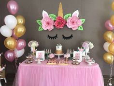 a table topped with lots of pink and gold balloons next to a unicorn face cake