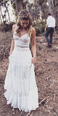 a woman in a white dress is walking through the woods with a man behind her