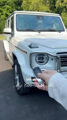 a person is holding a remote control in front of a white mercedes g - class