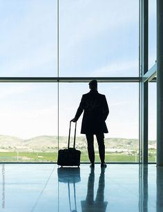 a man with a suitcase standing in front of a large window by an airport terminal