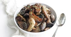 a white bowl filled with mushrooms on top of a table next to two spoons