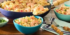 two bowls filled with macaroni and cheese on top of a wooden table next to utensils