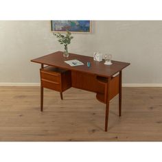 a wooden desk with two drawers and a vase on it's side, in front of a white wall