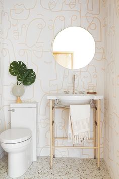 a white toilet sitting next to a sink in a bathroom under a large round mirror