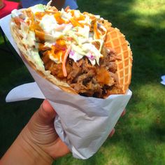 a hand holding a waffle filled with meat and coleslaw on top of it