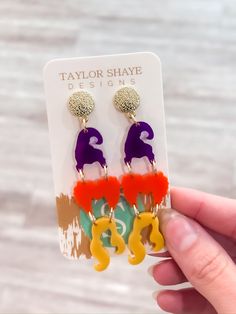 a pair of colorful earrings is being held by a person's hand on a white background