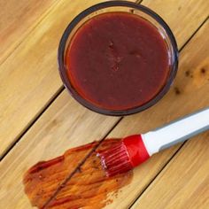 a cup of sauce sitting on top of a wooden table next to a paintbrush