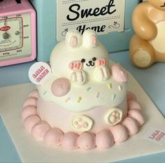 a white cake with pink icing and teddy bears on the top is sitting on a table