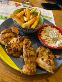 a plate with chicken, french fries and coleslaw on it next to a bowl of potato wedges