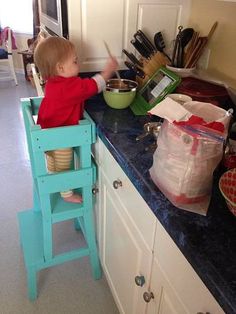 a toddler sitting in a high chair at the kitchen counter with bowls and utensils