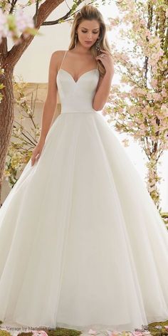 a woman in a white wedding dress standing next to a tree with pink flowers on it