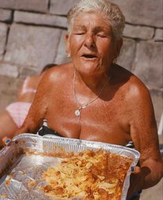 an older woman holding a pan filled with food