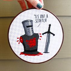 someone is holding up a cross - stitch hoop with a drawing of a knife and a bottle on it