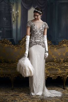 a woman standing in front of a couch wearing a white dress with feathers on it