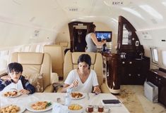 two people sitting at a table with plates of food in front of them on an airplane