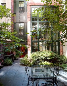 an outdoor dining table and chairs in front of a brick building with green doors on the windows