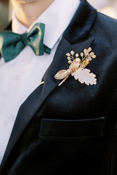 a man wearing a black suit with a green bow tie and gold leaf brooch