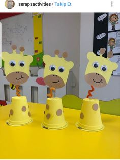 three giraffes made out of construction paper cups on a yellow table top