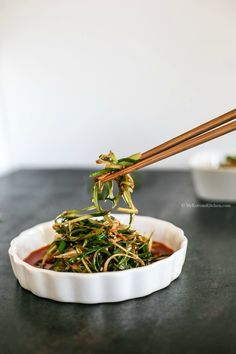 chopsticks picking up some food from a white bowl on a black countertop