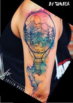 a watercolor tattoo on the arm of a woman with mountains and trees in a hot air balloon