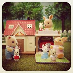 a group of toy animals standing in front of a doll house with a rabbit on the roof