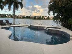 an empty swimming pool surrounded by palm trees next to the water with lounge chairs around it