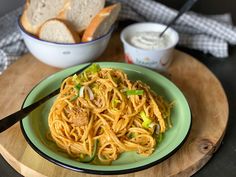 a green plate topped with pasta and bread next to a bowl of dips on a wooden tray