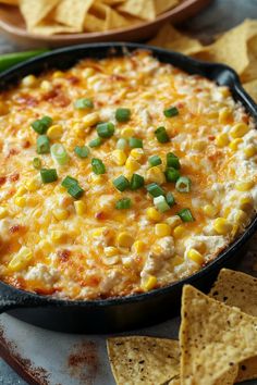 a black pan filled with corn and cheese next to tortilla chips