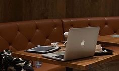 an open laptop computer sitting on top of a wooden table next to a brown bench