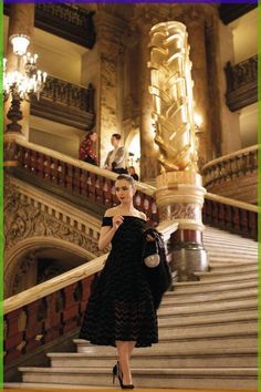 a woman in a black dress is walking down the stairs with her hand on her hip