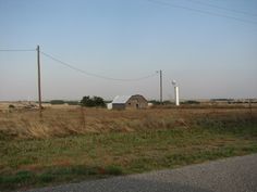 an old barn sits in the middle of a field with power lines and telephone poles