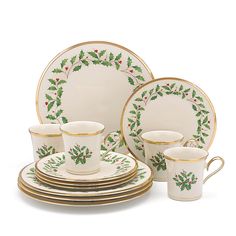 a white and gold christmas dinnerware set with holly designs on the rims, cups and saucers