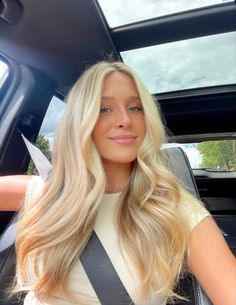 a woman sitting in the back seat of a car with long blonde hair and blue eyes