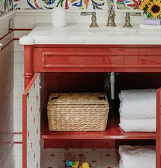 a red cabinet with towels and toys in the bottom shelf, next to a sink