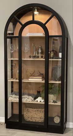 an arched glass display case with many items on it's shelves in front of a wall