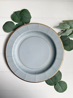 a white plate with gold trim surrounded by green leafy branches on a white background