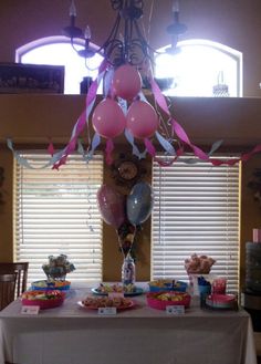 a table topped with balloons and cake next to a window covered in pink streamers