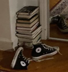 a pile of books sitting on the floor next to a pair of black converse shoes