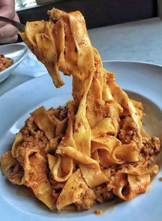 a plate with pasta and meat being lifted from the top by a fork to eat it