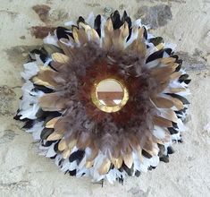 a decorative mirror with feathers on it sitting on a stone wall next to a brick wall