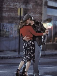 a man and woman standing in the street kissing each other with their arms around one another