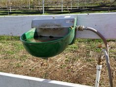 a green bowl hanging from the side of a white fence with a hose attached to it