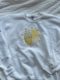 a white sweatshirt with yellow and grey designs on it's chest, sitting on a bed