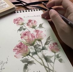 a person is holding a pen and drawing flowers on a notebook with watercolor paper