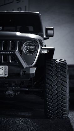 the front end of a black jeep parked in a parking lot with it's lights on