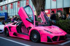 a pink sports car parked in front of a building with its doors open and people looking at it