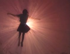 a girl is jumping in the air with her arms spread out and sunbeams behind her