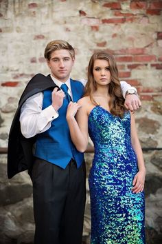 a young man and woman dressed up in formal wear posing for a photo with a brick wall behind them