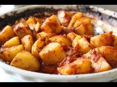 a white bowl filled with cooked potatoes covered in marinara sauce on top of a table